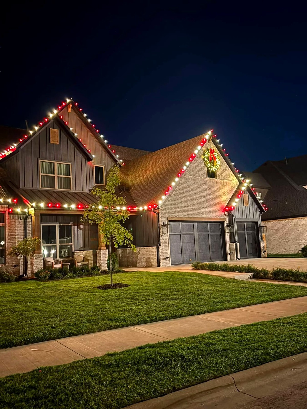 Two-story home with red and white roofline Christmas lights and a lighted wreath at night